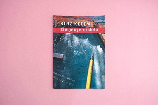 Knjiga "Blaž Kocen - Življenje in delo" ima naslovnico s svinčnikom in starim atlasom na rožnati podlagi.