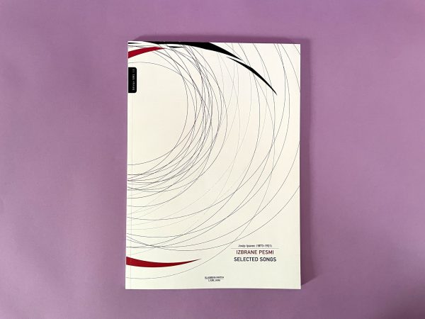 Knjiga z naslovom "Josip Ipavec, Izbrane pesmi/Selected songs" (Josip Ipavec, Izbrane pesmi) z belo platnico s tankimi črnimi in rdečimi ukrivljenimi črtami je postavljena na vijolično površino.