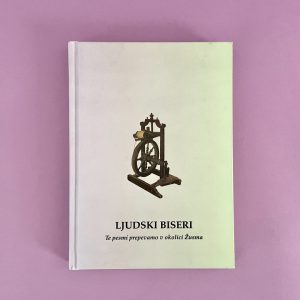 Bela knjiga z naslovom "Ljudski biseri" z ilustracijo kolovrata na naslovnici leži na rožnati površini. Podnaslov je v manjšem besedilu pod naslovom.