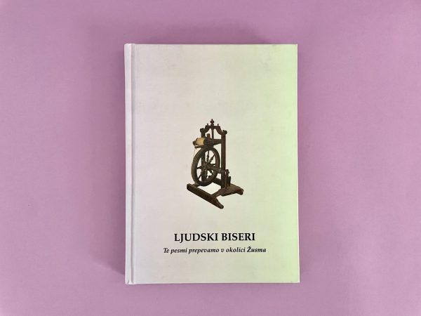 Bela knjiga z naslovom "Ljudski biseri" z ilustracijo kolovrata na naslovnici leži na rožnati površini. Podnaslov je v manjšem besedilu pod naslovom.