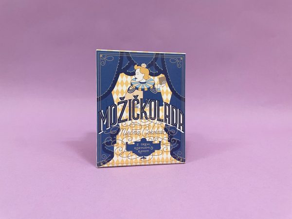 Na živahni škatli z napisom Možičkolada je stilizirana ženska s pijačo v roki na modrem in rumenem geometrijskem ozadju na vijolični površini.