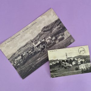 Dve starinski črno-beli fotografiji "Arhivska razglednica Sv. Jurij ob Južni železnici", ki prikazujeta mestece in cerkev, sta postavljeni pod kotom na pastelno vijolično ozadje in se rahlo prekrivata.