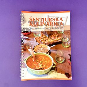 Na naslovnici kuharske knjige Šentjurska kulinarika so na vijoličnem ozadju lonec juhe, skleda riža in pekač na mizi s kozarci.