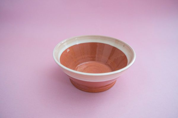 Skleda lončena, keramična skleda z rdečkasto rjavo notranjostjo in belim robom, je prikazana na rožnati površini z ustrezno rožnato podlago.