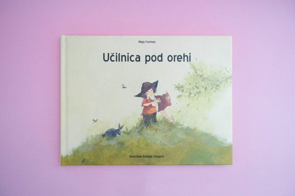 Knjiga z naslovom "Učilnica pod orehi" s karikaturo deklice, ki bere knjigo.